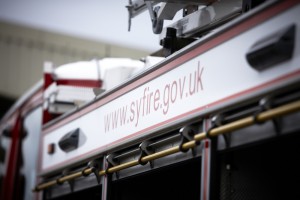 This picture shows the side of a fire engine. Specifically it shows a white strip above the three equipment lockers. The service's website address is written across the strip.