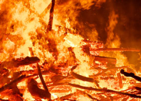 A large bonfire, made up of wood pallets and sticks, burns.