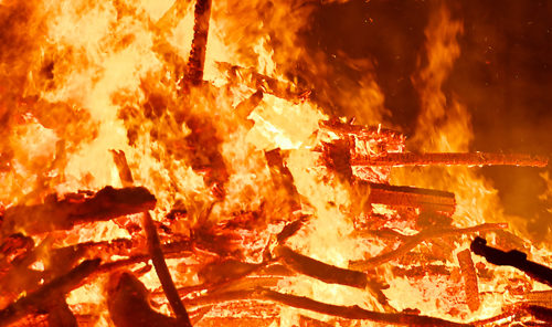A large bonfire, made up of wood pallets and sticks, burns.